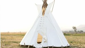 Een witte tipi met een centrale ingang, midden in een begraast veld met weinig beplanting.