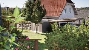 Il s’agit d’une propriété résidentielle dotée d’un jardin bien entretenu, d’une terrasse en bois et d’une maison avec un toit recouvert de tuiles rouges.