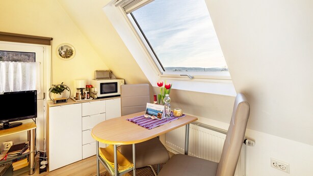 A compact kitchenette with a microwave, a small table with a placemat, a chair, and a window with a view. - Studio Casa Felicitas, 1 living/sleeping room, max. 2 guests (not suitable for young children or dogs) (Möhnesee)