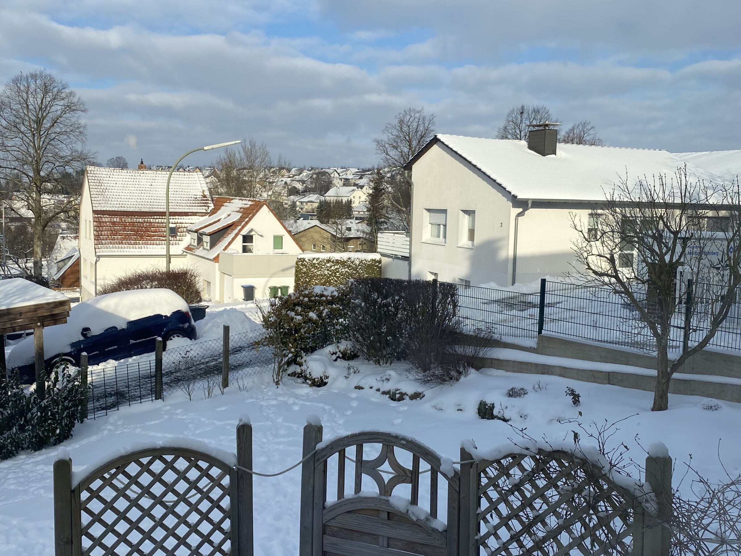 A residential area with houses, a snow-covered car, and a wooden gate.