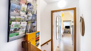 A hallway with a bulletin board displaying various travel brochures and a wooden staircase leading to another room. - Studio Casa Felicitas, 1 living/sleeping room, max. 2 guests (not suitable for young children or dogs) (Möhnesee)