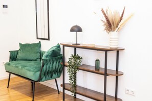 A room with a green upholstered chair, a wooden console table with a lamp, and a vase with dried plants. - City of Rastatt—Stylish Living in a Historic Building (Rastatt)