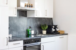 A modern kitchen with white cabinets, a black countertop, a coffee machine, and a plant. - City of Rastatt—Stylish Living in a Historic Building (Rastatt)