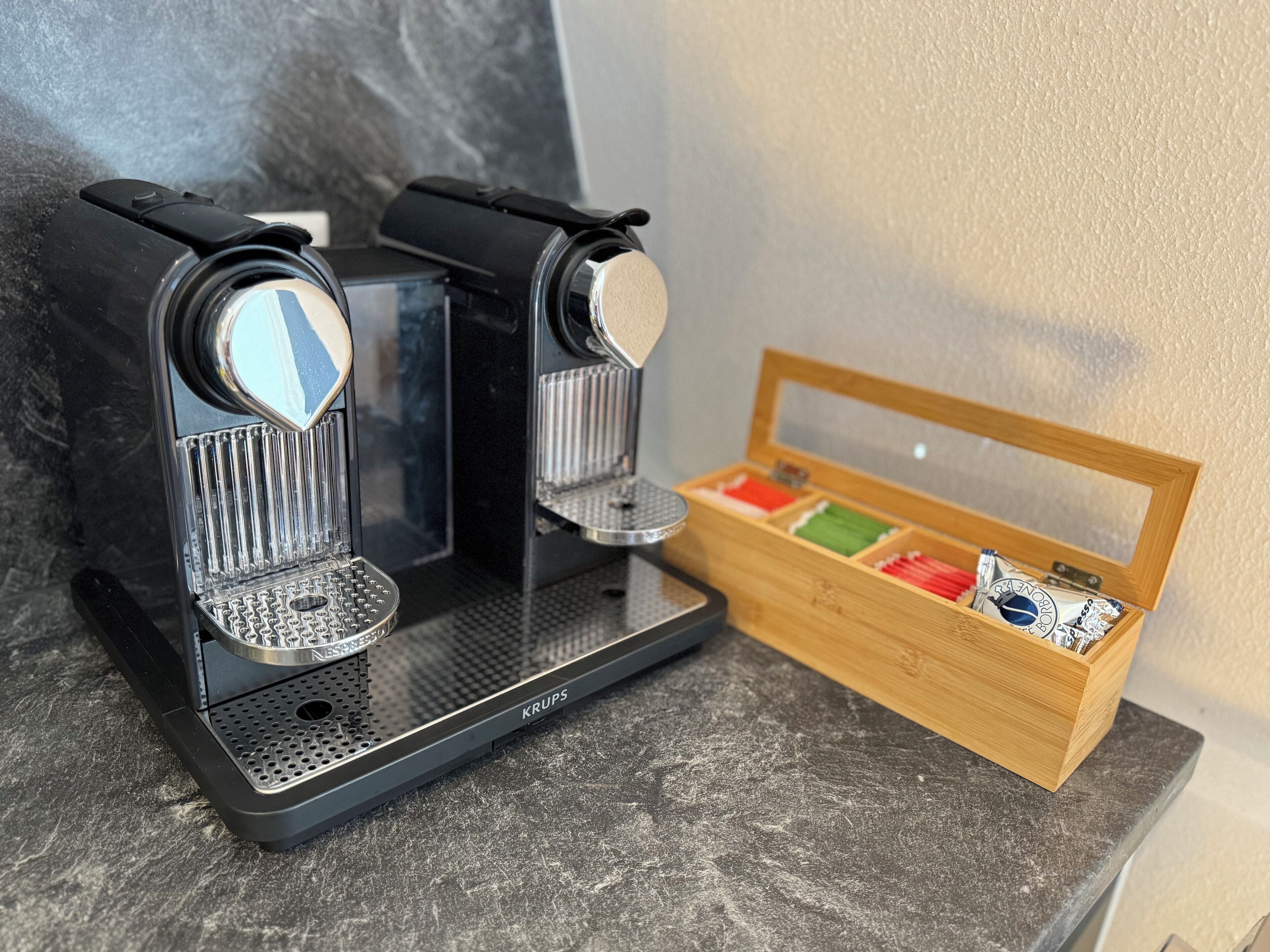 A Krups espresso machine on a countertop with a wooden box containing colorful capsules.