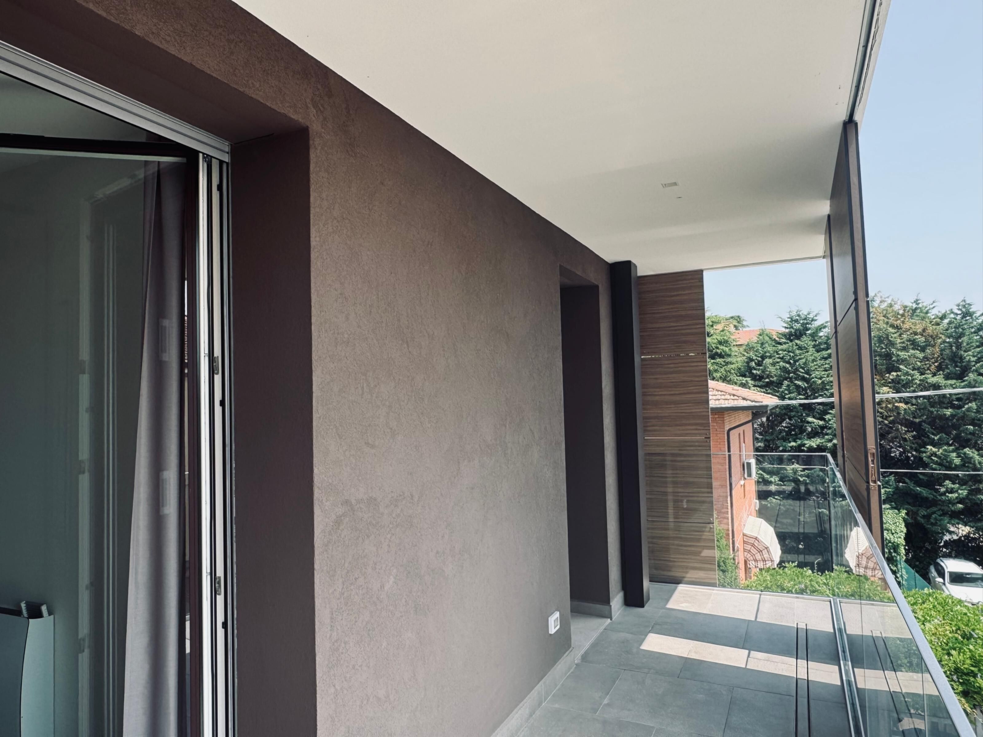 Ein moderner Balkon mit Glastür, einer Betonwand und Blick auf ein Wohngebiet.