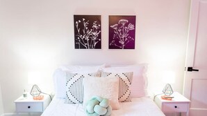 Une chambre à coucher bien rangée, avec un lit, deux tables de chevet et deux tableaux représentant des fleurs, accrochés au mur.