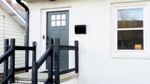 Une maison avec une porte d’entrée grise, une petite fenêtre et une rambarde en métal noir sur les marches extérieures.