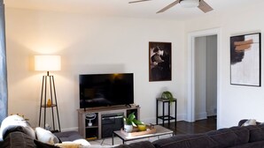 Un salon équipé d’un téléviseur à écran plat, d’un ventilateur de plafond, d’un canapé et d’une table basse agrémentée d’objets décoratifs.