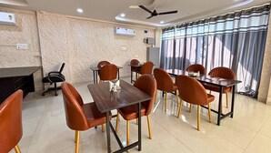 A conference room with a long table, several chairs, ceiling fans, and a large window with curtains. - The Mayfair Hotel (Indore)