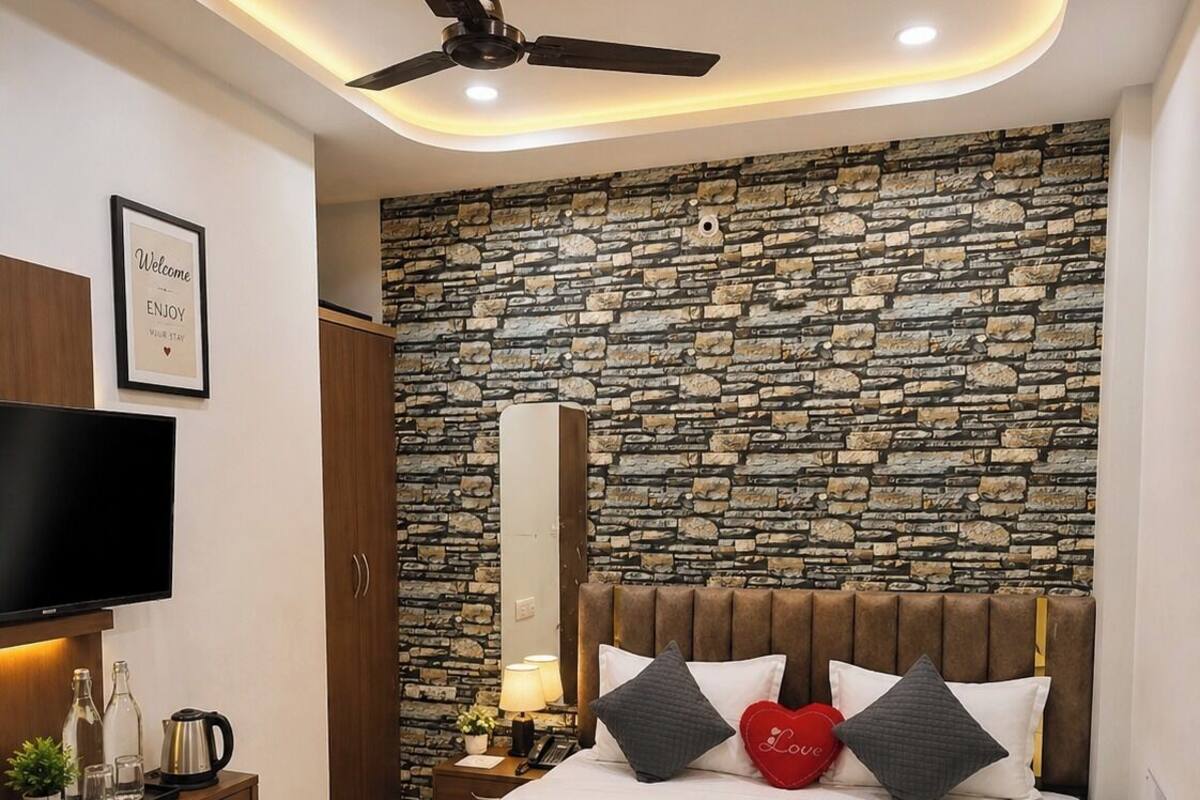 A modern hotel room with a stone wall, a flat-screen TV, a bed with a headboard, bedside tables, and a ceiling fan.