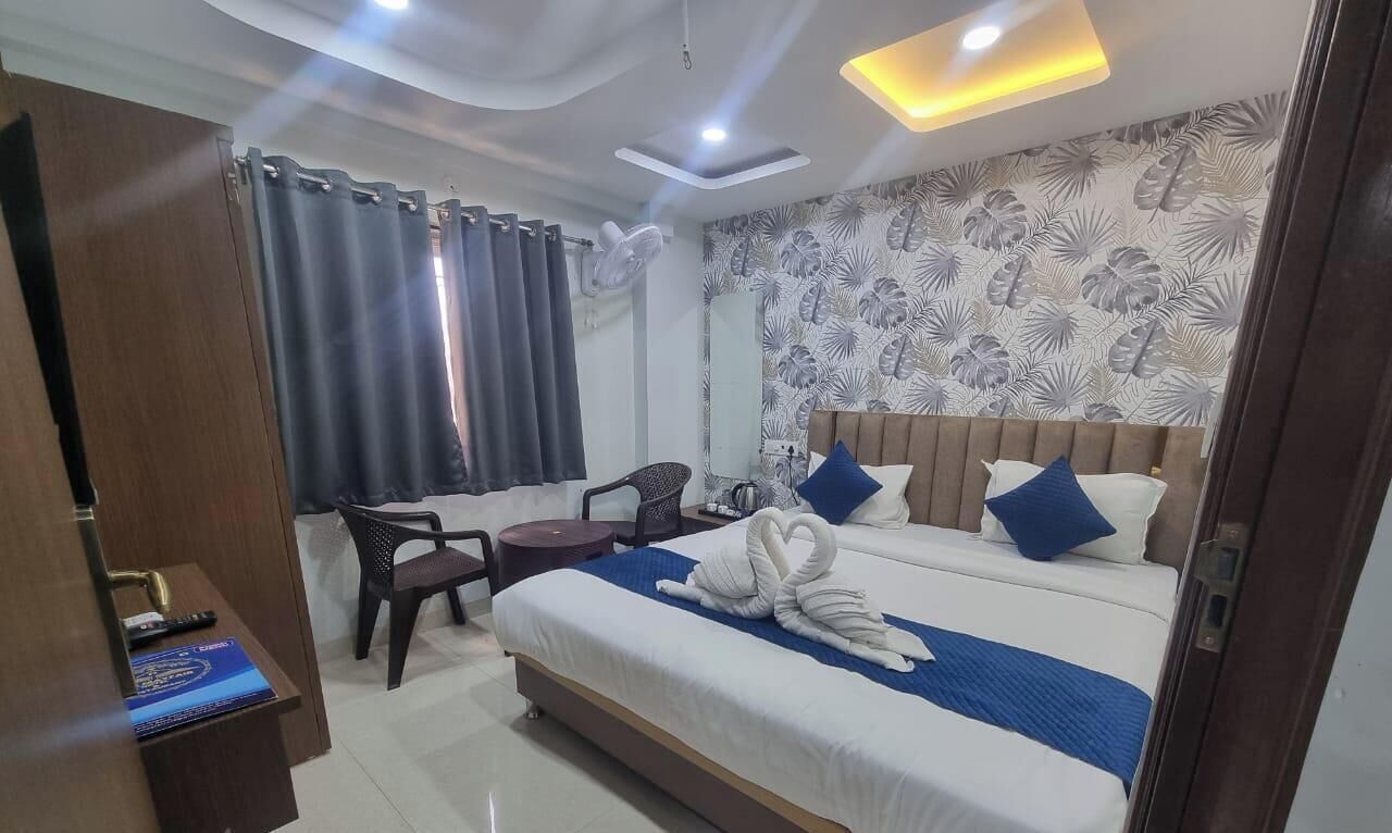 A hotel room with a bed, a desk, a chair, a fan, and a window with curtains.