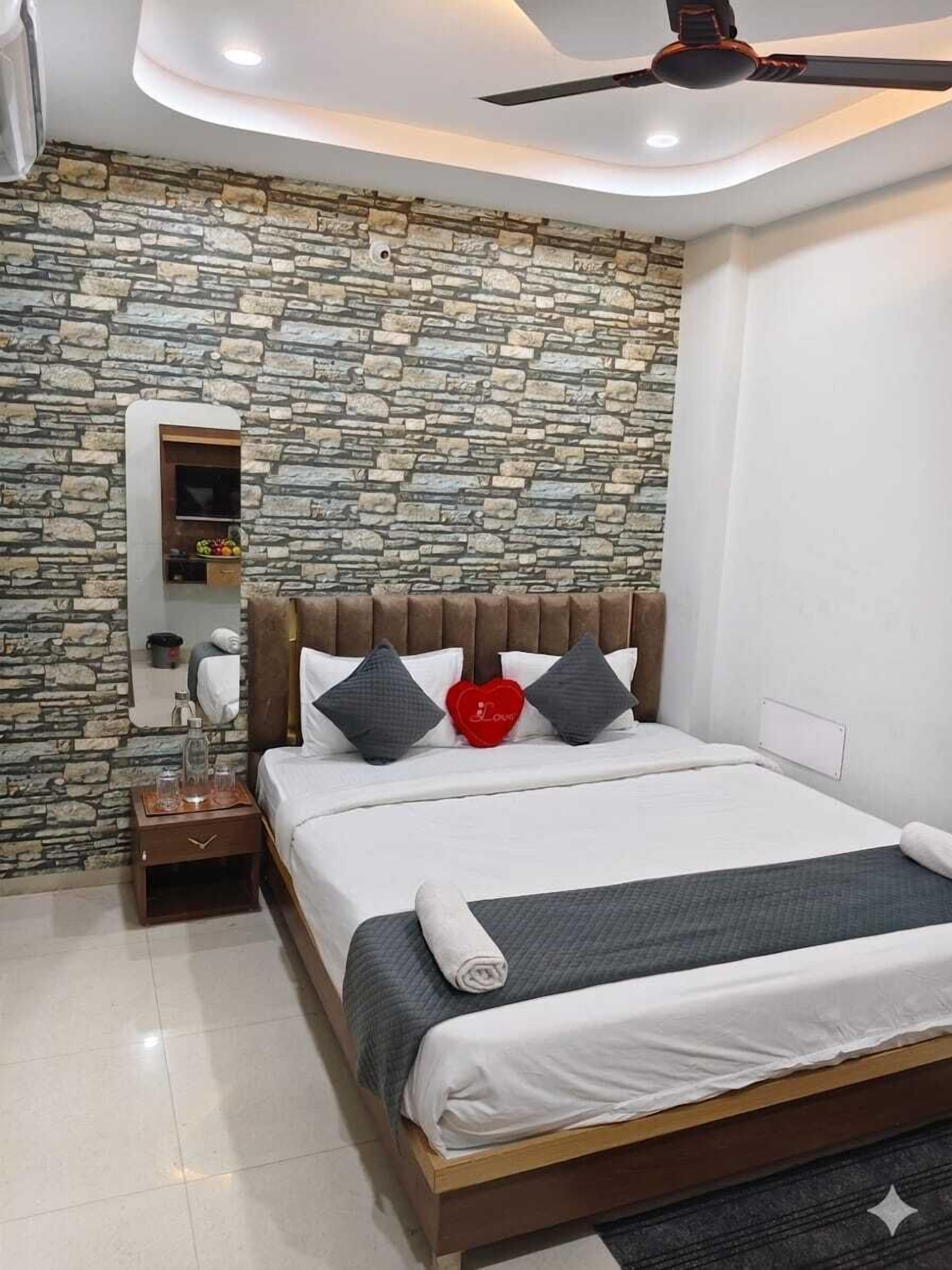 A bedroom with a stone wall, a bed with a wooden headboard, a nightstand, and a ceiling fan.