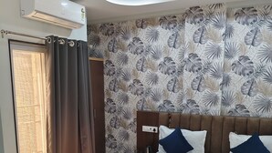 A hotel room with a bed, curtains, a ceiling fan, and a wall with a leaf pattern. - The Mayfair Hotel (Indore)