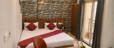 A bedroom with a stone wall, a bed with red pillows, a wooden headboard, a chair, a small table with a tray, and a window with curtains.