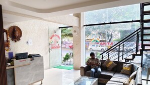 A hotel lobby with a reception desk, a sofa, a glass coffee table, and a staircase leading outside. - The Mayfair Hotel (Indore)