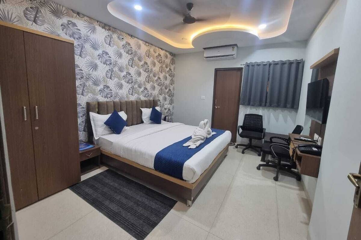 A hotel room with a bed, a desk, a chair, an air conditioning unit, and a ceiling fan.
