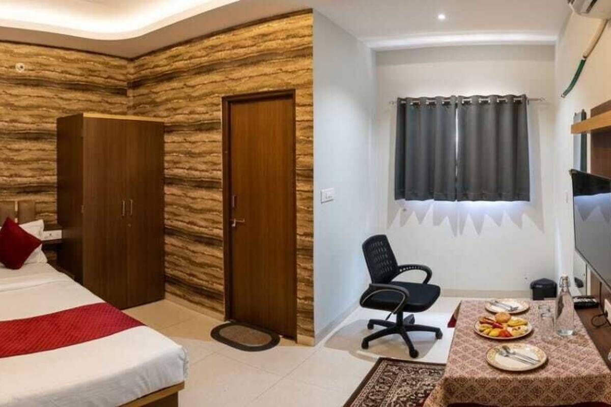 A hotel room with a bed, wardrobe, desk, chair, television, and a window with curtains.