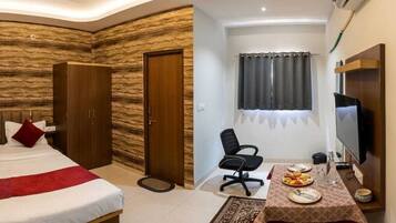 A hotel room with a bed, wardrobe, desk, chair, television, and a window with curtains.