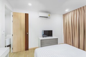 Ein Hotelzimmer mit einem Bett, einem Fernseher auf einer Kommode, einer Klimaanlage, einer Holztür und beigen Vorhängen.
