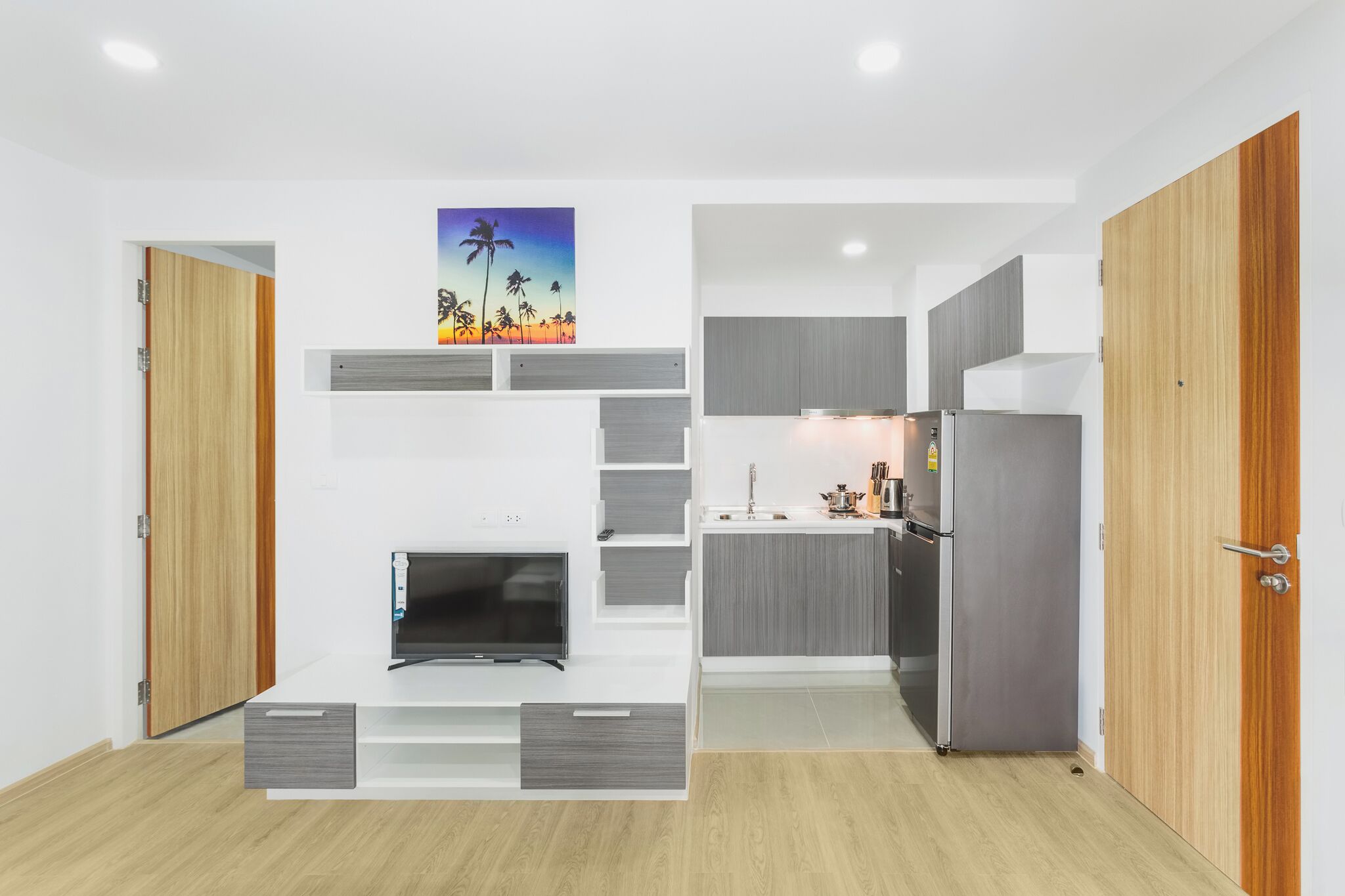 A compact kitchen with a built-in TV, grey cabinets, and a refrigerator.