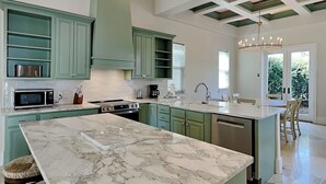 A spacious kitchen with teal cabinetry, a marble island, and a large island with a sink. - Blue Mountain Bella (Santa Rosa Beach)