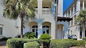 A white building with multiple balconies, arched doorways, and palm trees. - Blue Mountain Bella (Santa Rosa Beach)