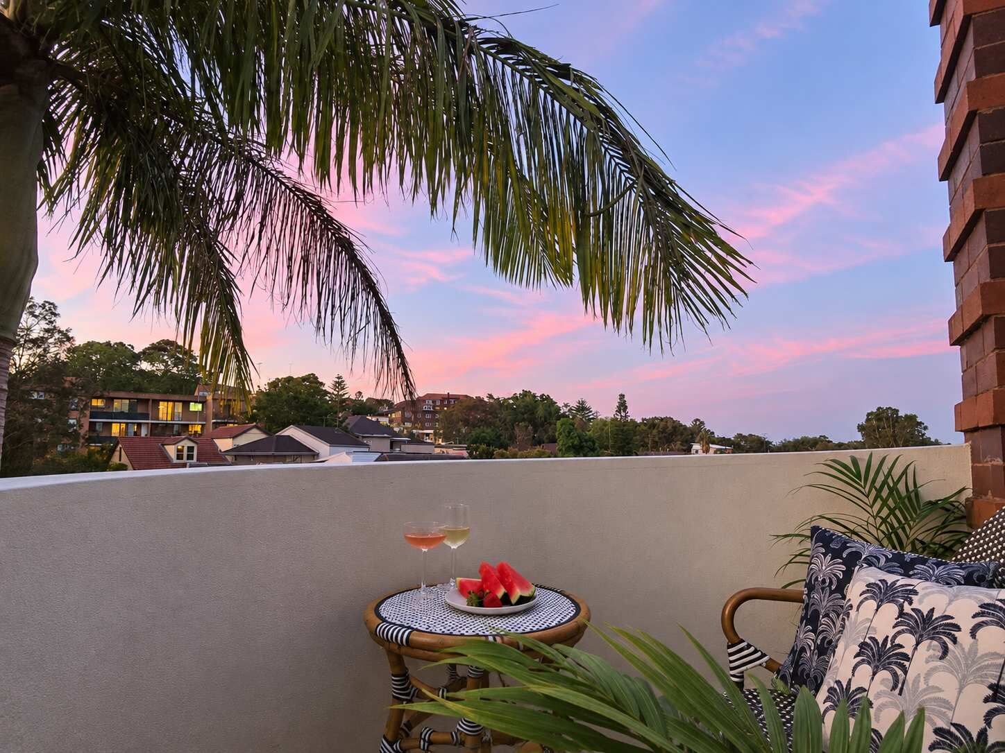 A rooftop terrace with a table set for two, a glass of wine, and a plate of watermelon.