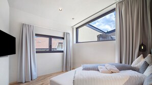 Une chambre avec une grande fenêtre, un lit avec des oreillers et un téléviseur à écran plat fixé au mur.