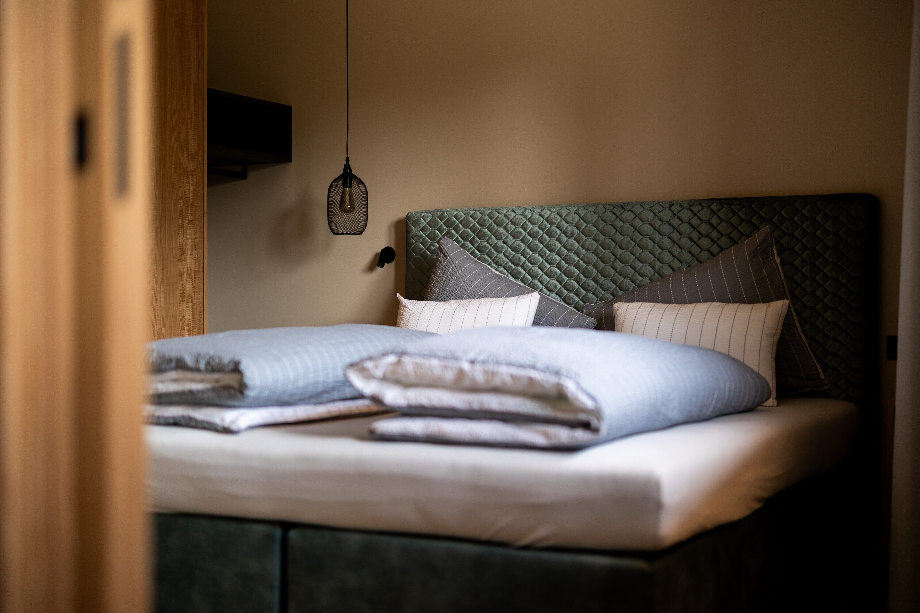 Un lit bien fait, avec des oreillers et une couverture, un luminaire suspendu et un cadre de porte en bois.