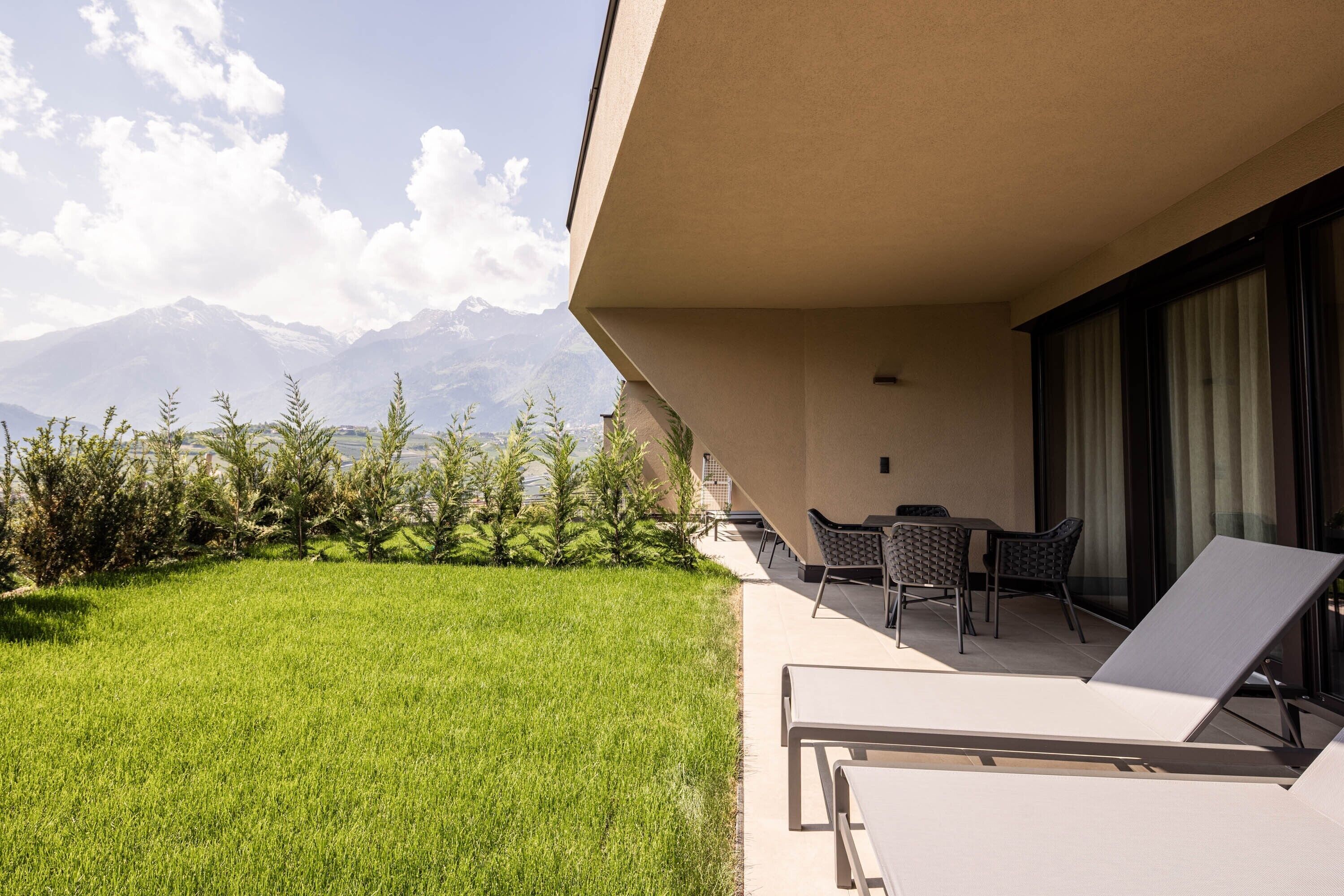 Un balcón con vistas a montañas, un espacio con césped y mobiliario exterior.