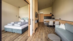 Un dormitorio moderno con cama, sofá, una mesita y una kitchenette al fondo.