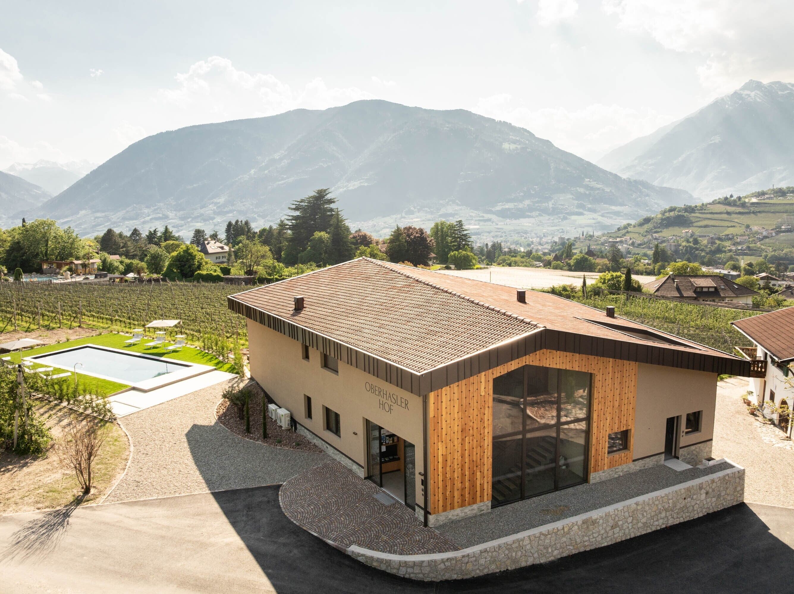 A modern building with a pool, surrounded by vineyards and mountains.