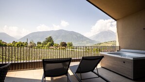 Un balcón con dos sillas, un jacuzzi y vistas a las montañas.