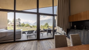 Une chambre moderne dotée d’une grande porte-fenêtre coulissante donnant sur un balcon avec vue sur les montagnes et le paysage urbain.