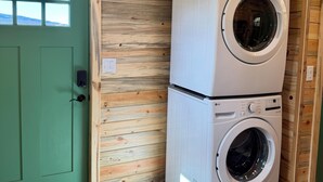 A laundry room with two stacked washing machines, a green door, and wooden walls.