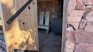 A rustic wooden door with metal hinges, leading to a stone-walled interior with a bench and a metal cabinet.