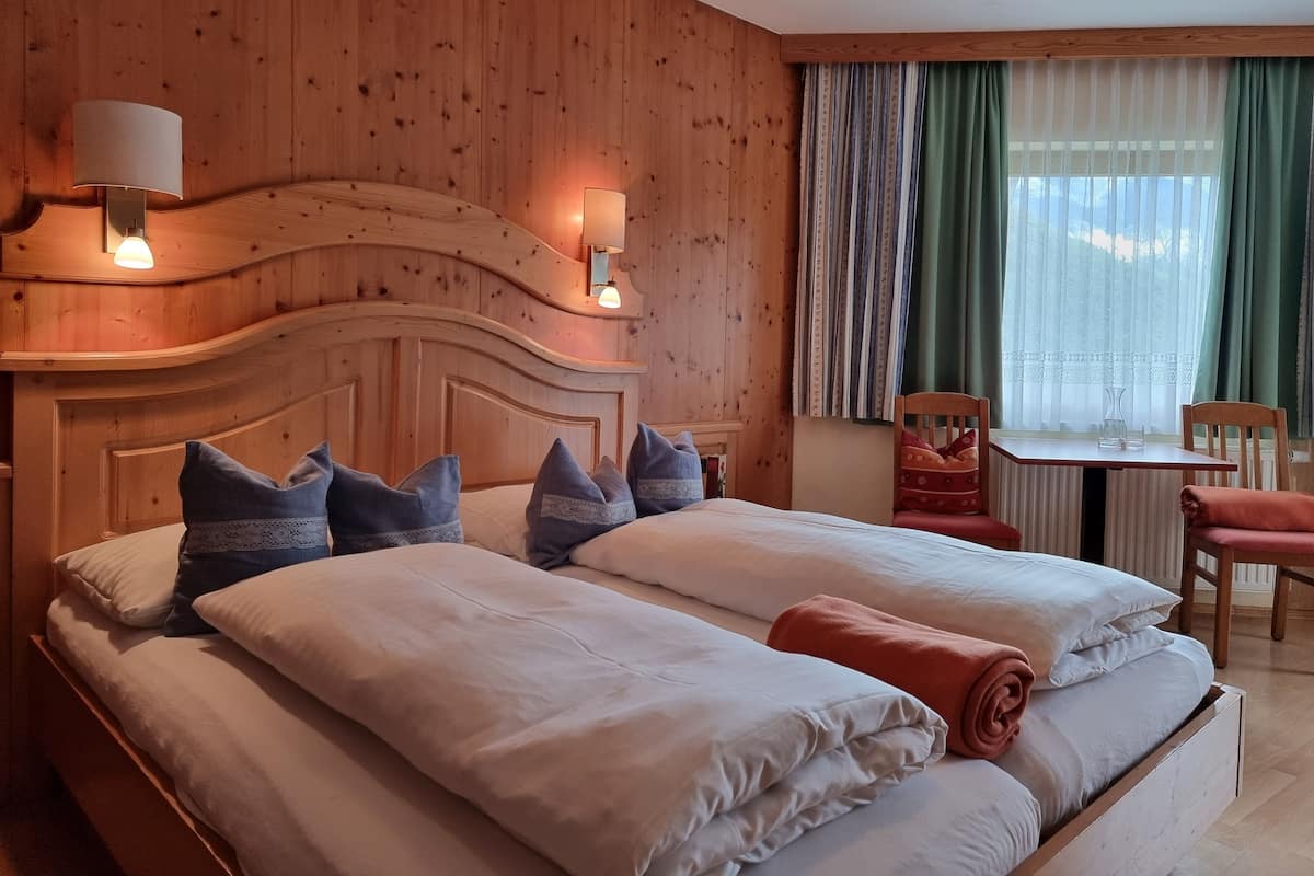 A double bed with pillows, a wooden headboard, a bedside table with a lamp, and a window with curtains.
