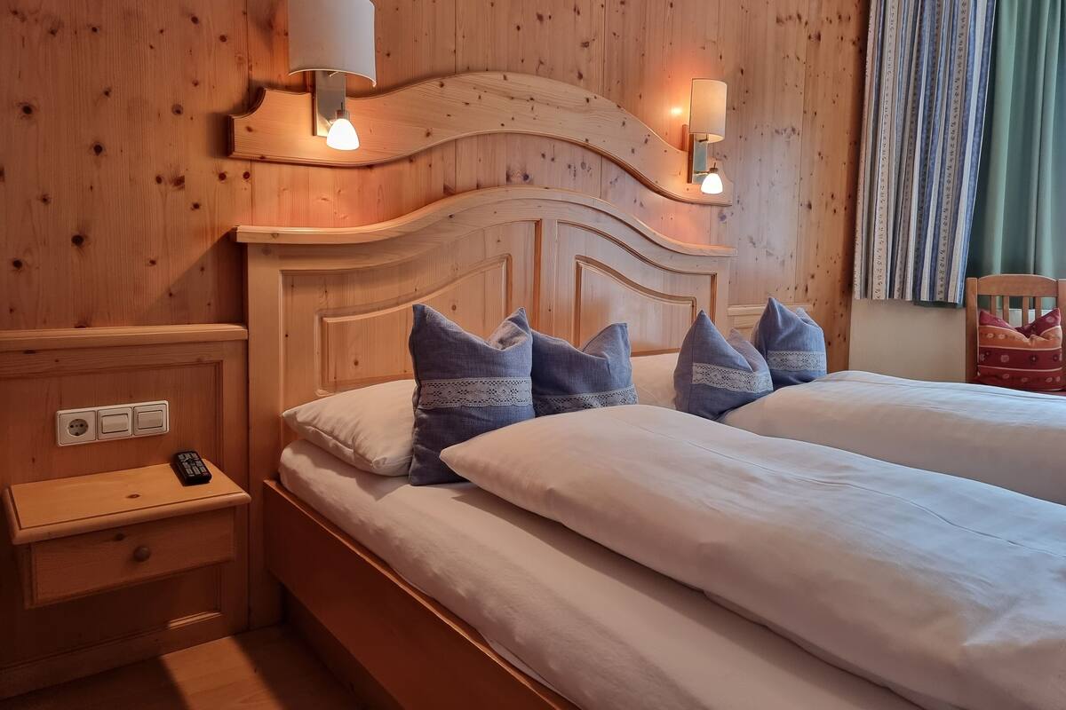 A double bed with a wooden headboard, two bedside lamps, and a nightstand with a remote control.