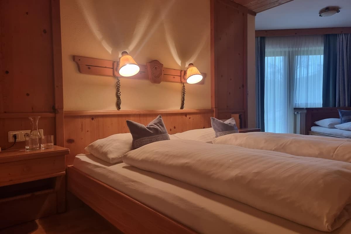 A hotel room with two beds, wooden headboard, bedside lamps, and a window with curtains.