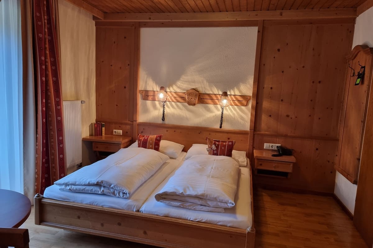 A wooden bedroom with a large bed, two bedside tables, a nightstand, and a wooden ceiling.