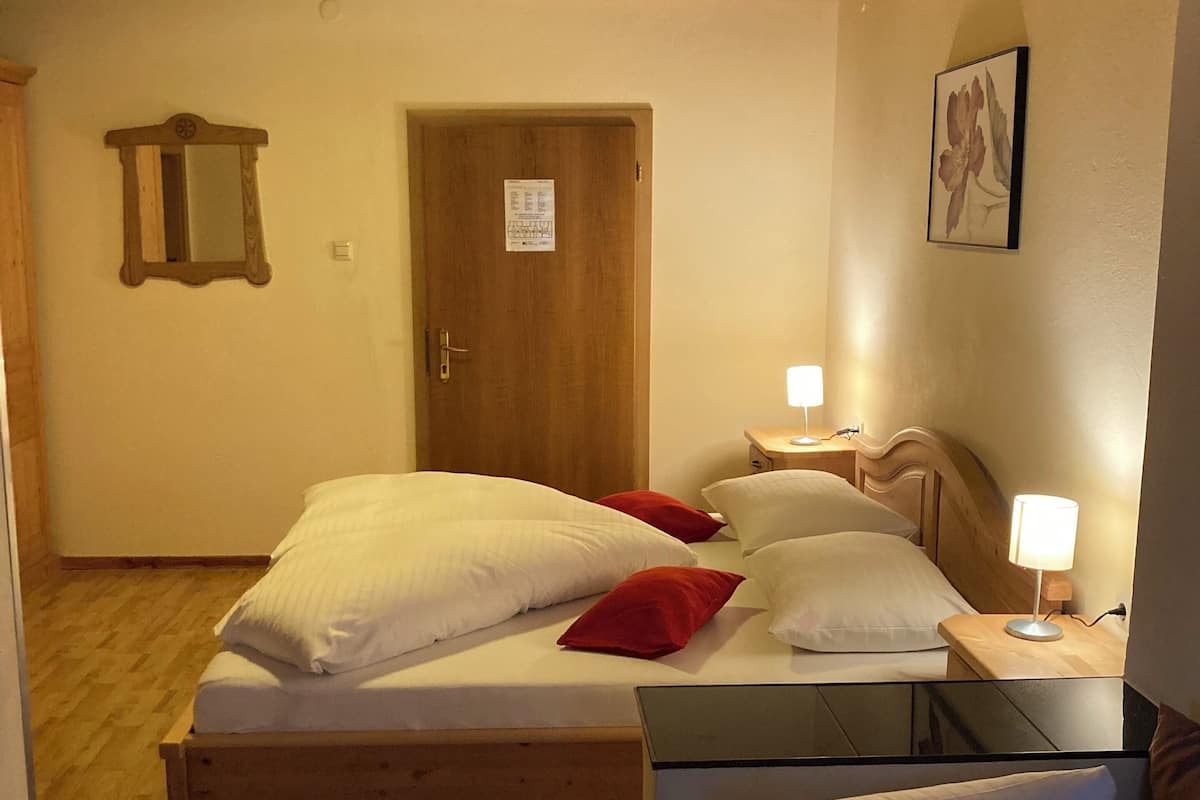 A bedroom with a wooden bed, a bedside table with a lamp, a mirror, and a door with a notice.