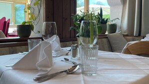 Una mesa de comedor dispuesta con cubiertos, vasos y una servilleta, con plantas en macetas y una lámpara de pared.
