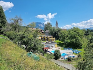 A hotel with a swimming pool, a church, and mountains in the background. - Hotel Karnischer Hof (Sankt Stefan im Gailtal)