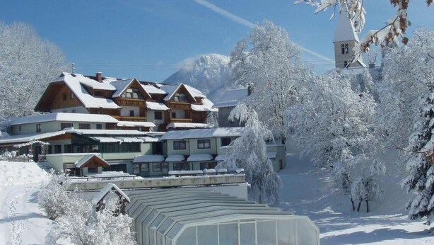 Un albergue cubierto de nieve con varias construcciones, un invernadero e iglesias al fondo.