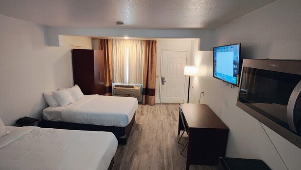 A hotel room with two beds, a desk, a TV, and a door leading to a bathroom. - Rodeway Inn & Suites Rancho Cordova - Folsom (Rancho Cordova)