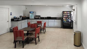 A kitchen with a dining table, chairs, a refrigerator, a coffee machine, and a vending machine.