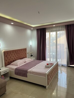 A modern bedroom with a large bed, a bedside table, a nightstand, and a view of the outside through sheer curtains.