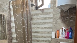 A bathroom with a shower, toilet, and sink. There are toiletries on the wall and a towel on the toilet. - Cityheart Apartments Ulcinj, Montenegro (Ulcinj Municipality)