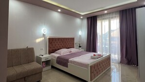 A modern bedroom with a bed, nightstands, a sofa, and a large window with curtains. - Cityheart Apartments Ulcinj, Montenegro (Ulcinj Municipality)