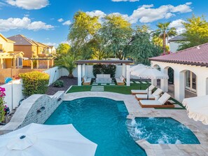 En privat pool med en stenbelagd terrass, solstolar och en pergola.